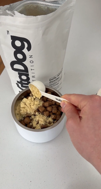 Hand scooping VitaDog powder supplement into a dog's food bowl